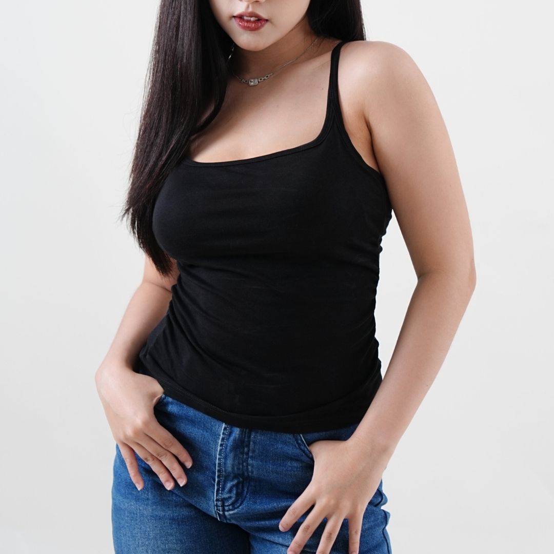 Woman wearing a black tank top and blue jeans on a plain background
