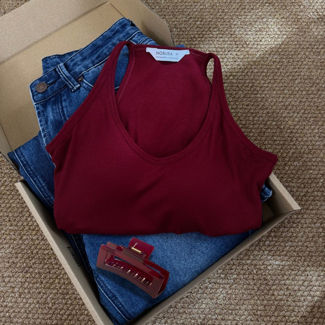 Folded red tank top and blue jeans in a cardboard box on a textured surface