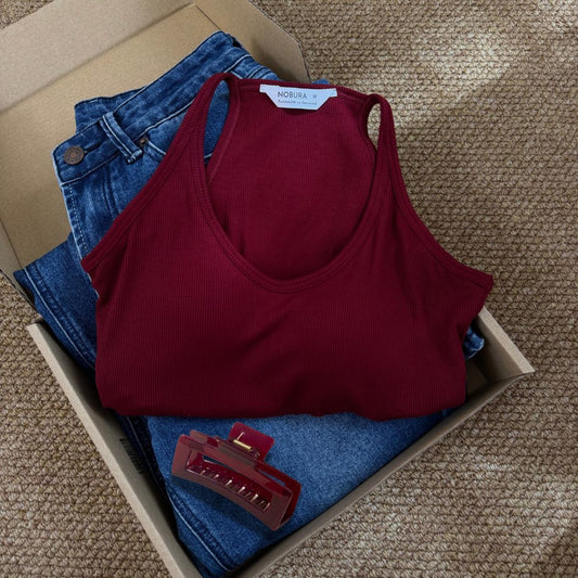 Folded red tank top and blue jeans in a cardboard box on a textured surface