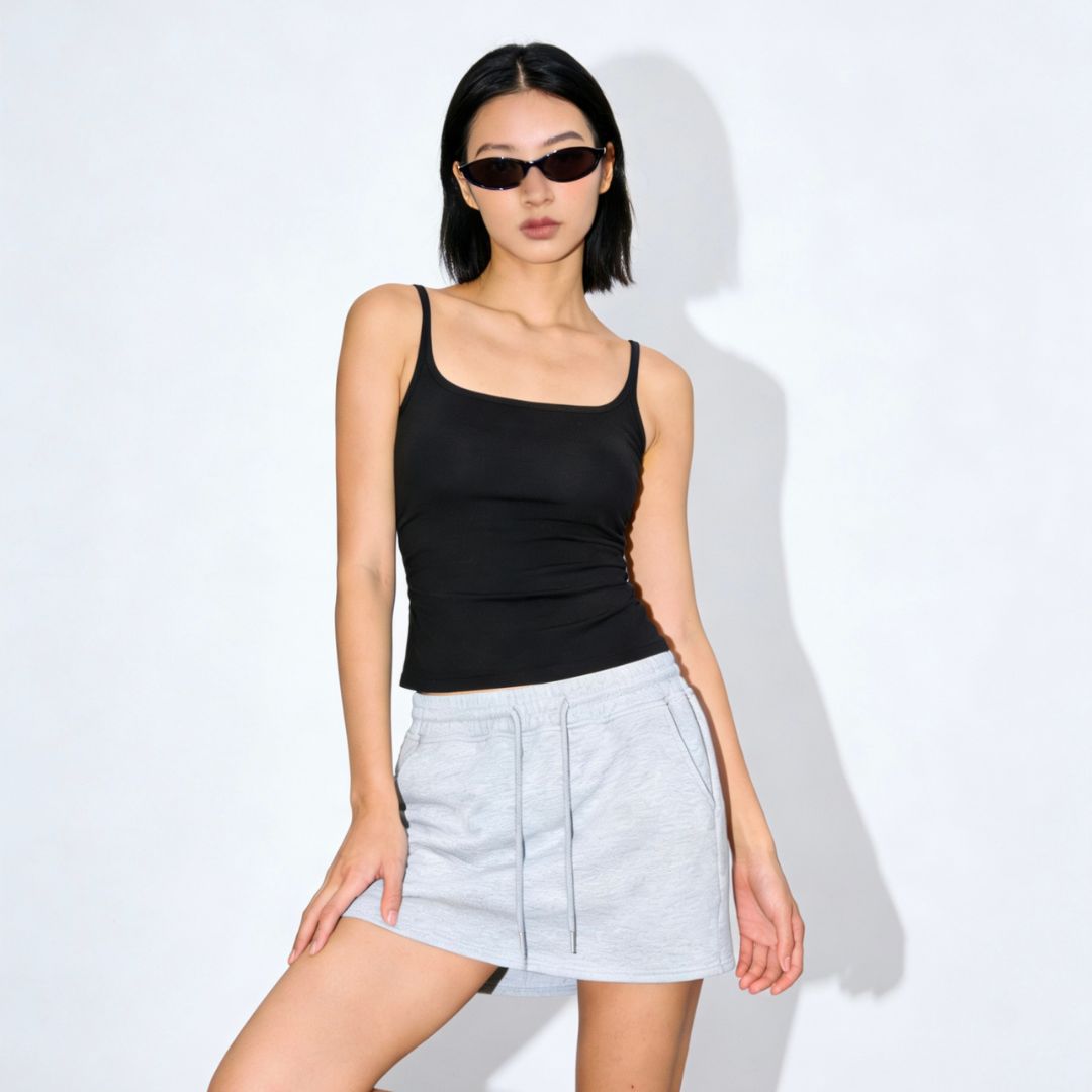 Woman wearing a black tank top and light blue shorts against a white background