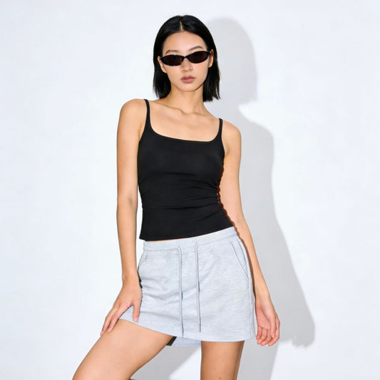 Woman wearing a black tank top and light blue shorts against a white background